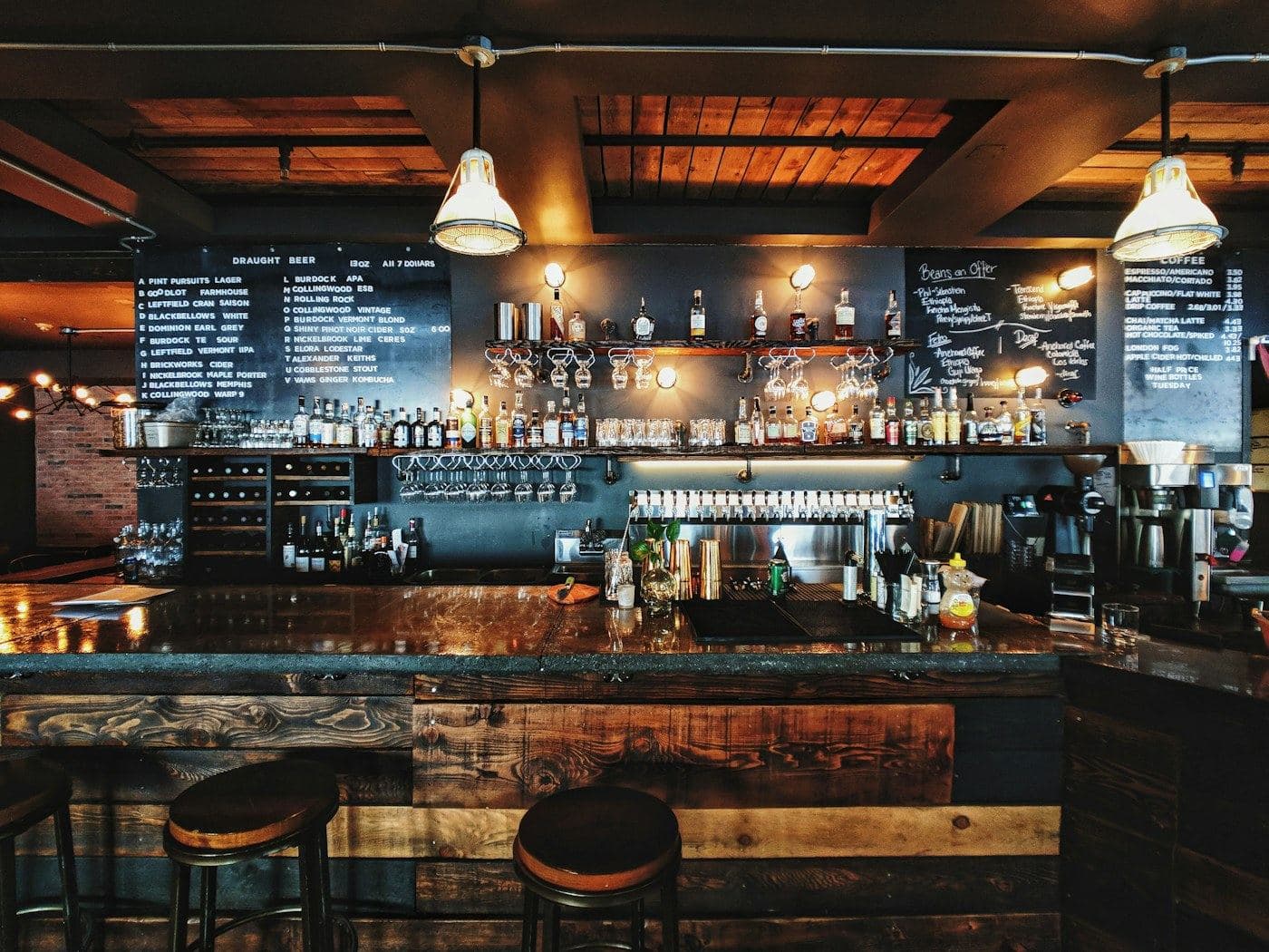 Bar counter backed by shelves of bottles and warm pendant lights