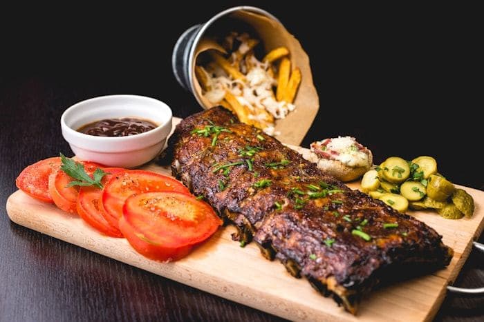 Rack of barbecue ribs on a wooden board with tomato and pickles