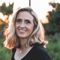 Woman with grey-blonde hair smiling outdoors at golden hour