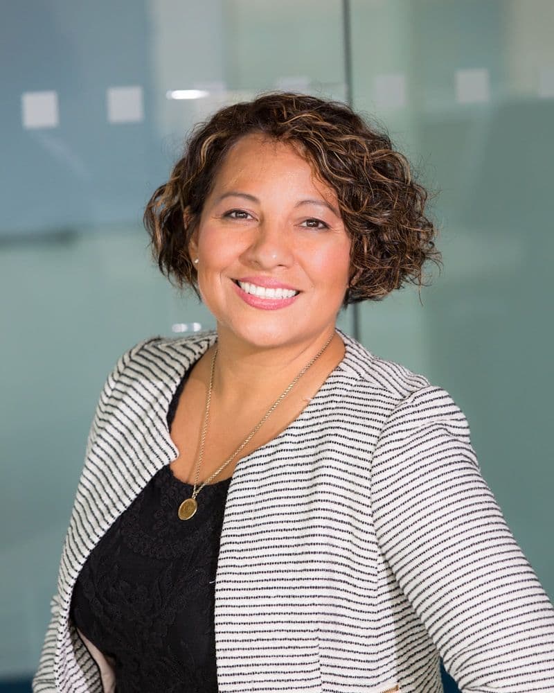 Aesthetician with short curly hair in a striped blazer, smiling