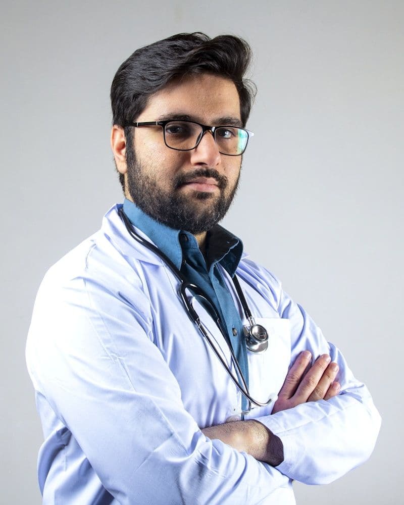 Doctor in a white coat and glasses standing with his arms folded
