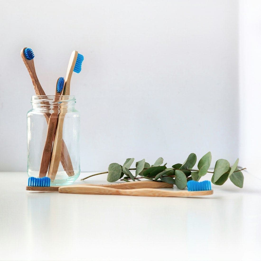 Bamboo toothbrushes in a glass jar beside eucalyptus